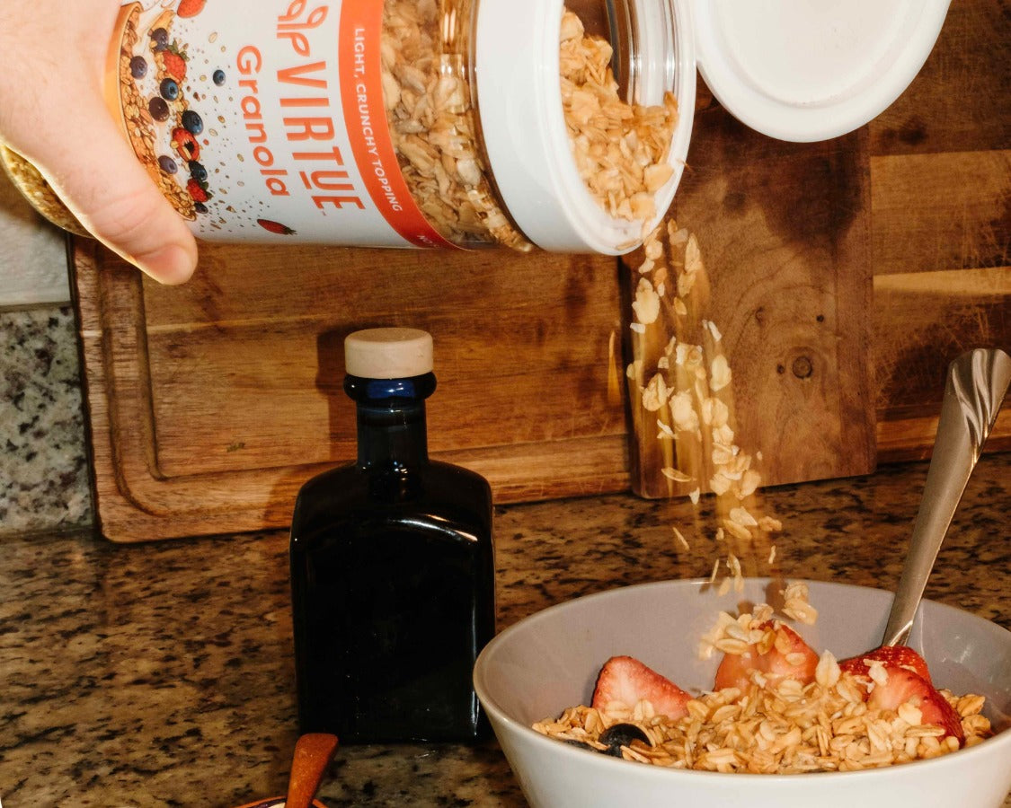 Virtue Granola shaker jar being poured onto a yogurt bowl
